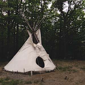 The brand-new teepee from the outside. There's a hammock outside and it's located in a clearing with plenty of room to live.