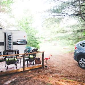 The outside of the camper- complete with a deck, picnic table, gas fire pit, and chairs.
