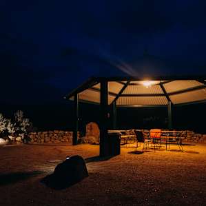 A gazebo by the lake has furniture, lights, and a fan to go out and enjoy some nature in the evening.