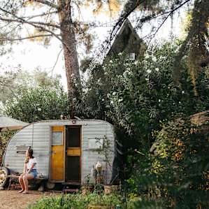 The trailer is nestled between an abundance of greenery and the A-Frame cabin.