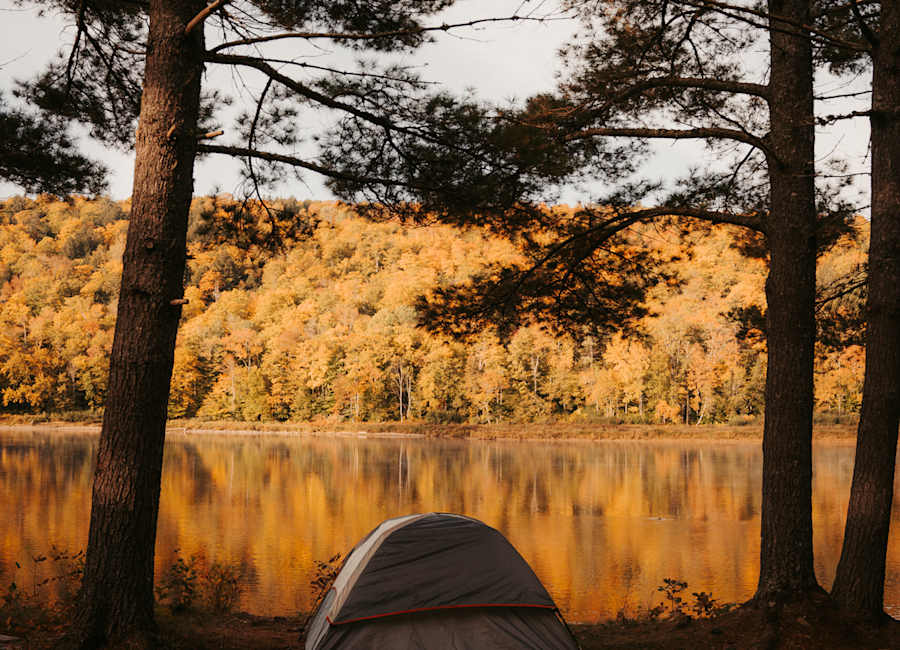 Tent beside a calm lake and gold autumn trees at Flashing Moose River Camping in Maine