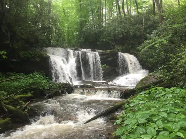 Multi-tiered waterfall cascading over rocks into a rushing stream surrounded by green forest