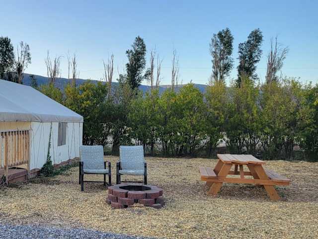 Canvas glamping tent with wooden deck and firepit at golden hour, mountains and trees behind