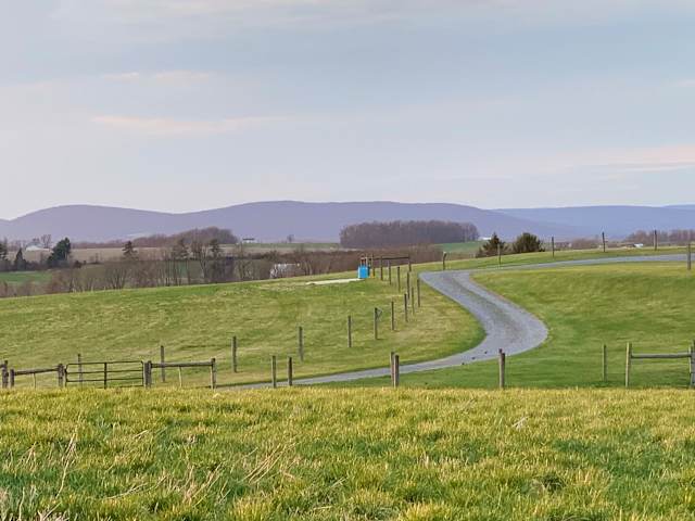 Gravel path curving through green pasture toward distant blue mountain ridges