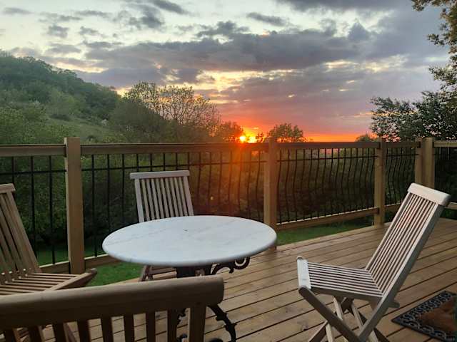 Wooden deck with table and chairs overlooking hills at sunset