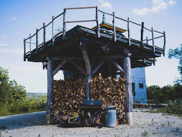 Elevated wooden platform with railing atop stacked firewood, overlooking distant hills