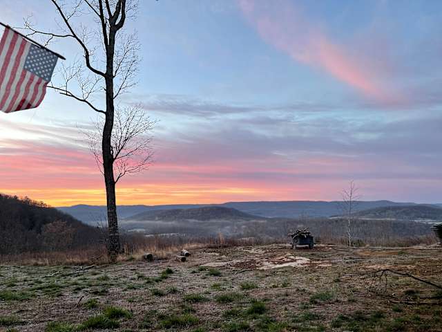 Bare tree and American flag silhouetted against pink sunset over layered Tennessee ridgelines