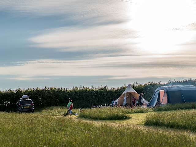 Campers and tents in a grassy field at sunset with hills beyond