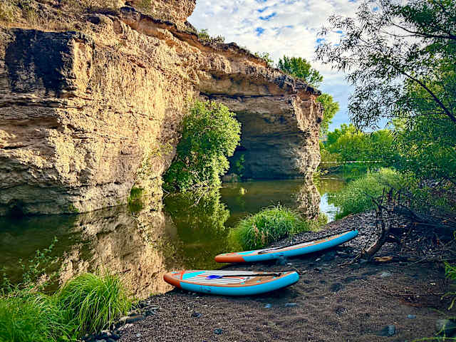 Sandstone rock arch over creek with two paddleboards resting on the bank