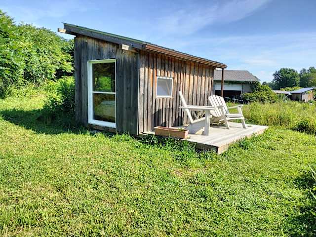 Rustic wooden cabin with deck and Adirondack chairs surrounded by green field