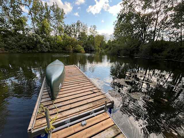 Wooden dock with a canoe extending into a calm, tree-lined pond