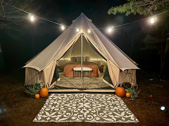 Bell tent illuminated at night with string lights and pumpkins under starry sky