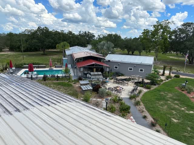 Aerial view of resort grounds with pool, red-roofed lodge, and lush trees under blue sky