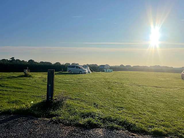 Camper van and tent glowing in golden sunrise light across open grass field