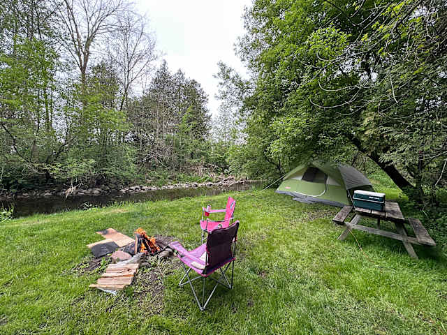 Green tent by riverside campsite with campfire, pink camp chair and picnic table