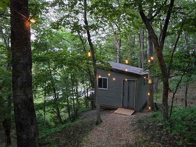 Small cabin lit by string lights along a path through dusk forest