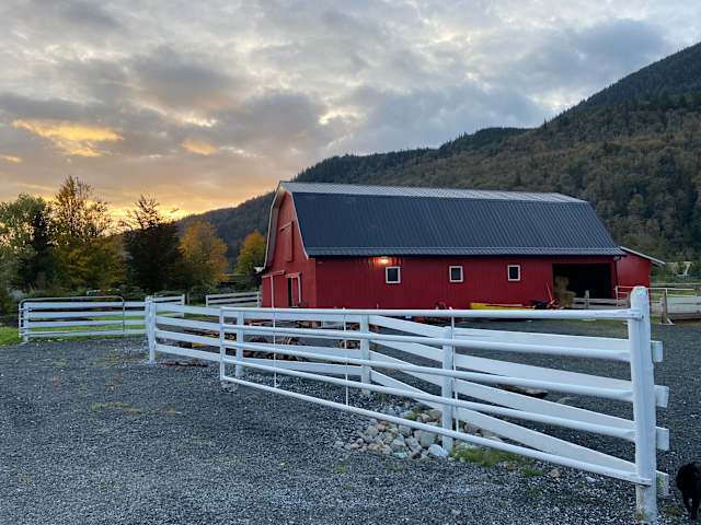 Red barn under dramatic sunset sky with white fence and forested mountains behind