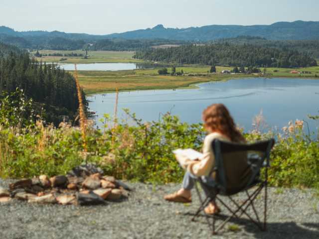 Grey Volkswagen camper van with pop-top open, overlooking lake and forested valley from gravel pad
