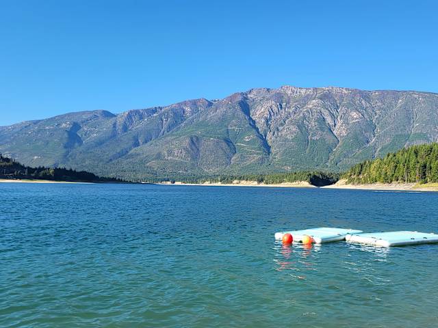 Aerial view of turquoise lake surrounded by forested mountains and distant snowy peaks