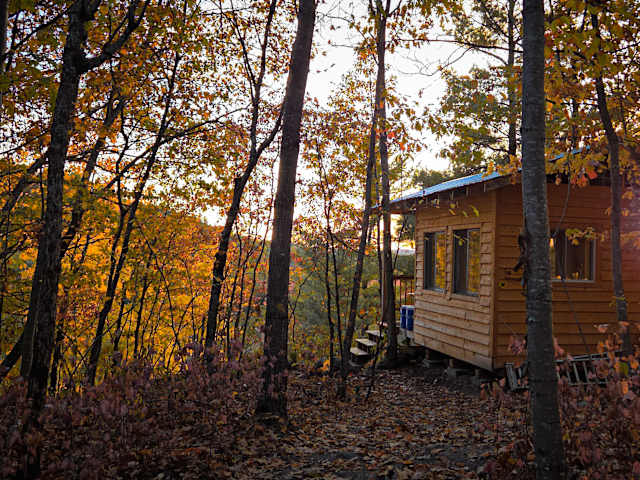 Small wooden cabin among autumn trees at sunset with warm backlight