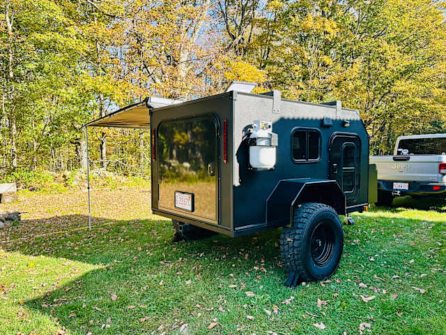 Small camper trailer with screened canopy parked beside a blueberry orchard
