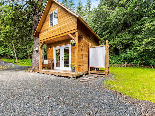 A-frame wooden cabin with porch and outdoor shower nestled among tall evergreen trees