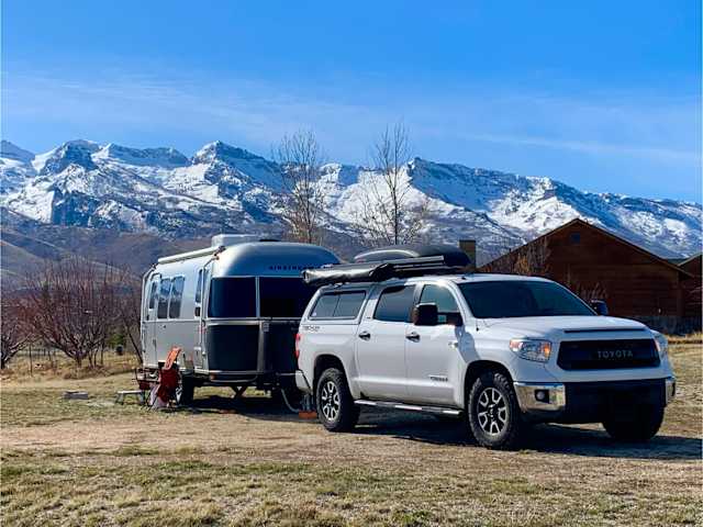 Airstream trailer and white pickup parked before snow-capped mountain range under blue sky