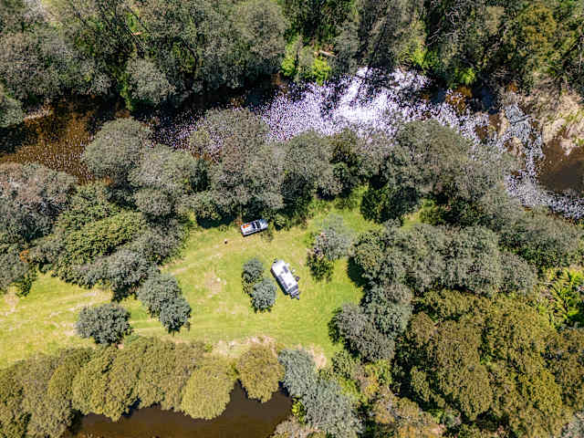 Aerial view of campervan and caravan on grassy riverside clearing surrounded by trees