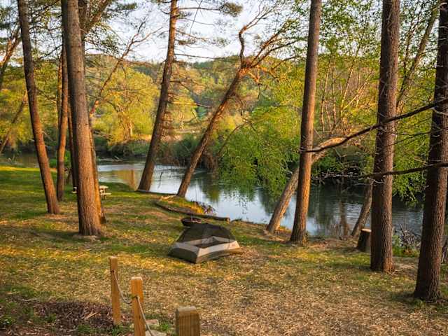 Tent pitched by a riverbank framed by tall pines at golden hour