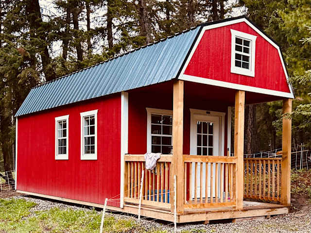 Red barn-style cabin with covered porch nestled among tall pine trees