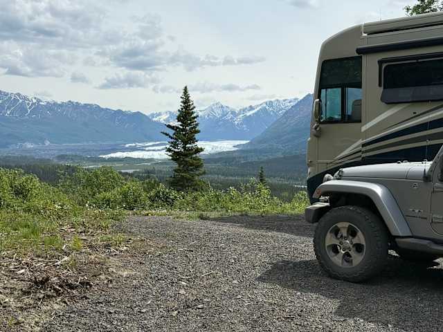 Jeep parked on gravel overlook with pine tree, glacier and snow-capped mountains beyond