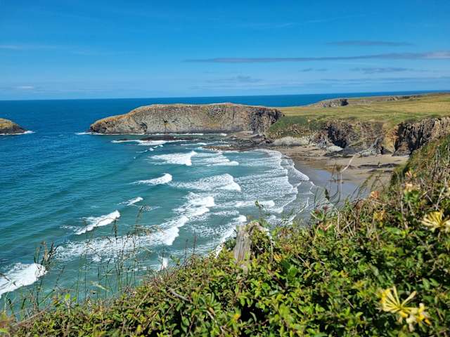 Turquoise sea meets sandy cove beneath green cliffs under clear sky