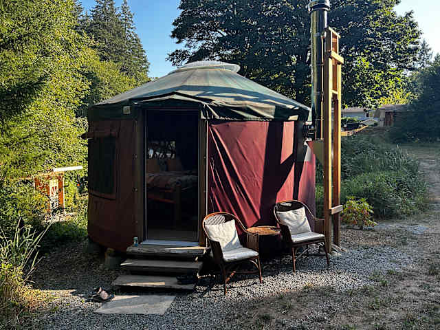 Maroon yurt with open door and wicker chairs in golden evening light among trees